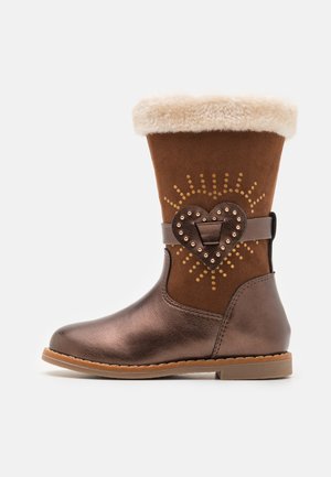 Botte en suede marron avec une partie inférieure en bronze métallique, un revers en fausse fourrure, une sangle décorative en forme de cœur et des motifs en points dorés sur le haut.
