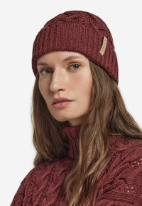 Bordowa dzianinowa czapka beanie o prążkowanej fakturze i wzorze warkocza, z małą skórzaną etykietą. Noszona na dopasowanym, dzianinowym golfie.