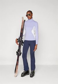 Σετ για σκι που περιλαμβάνει ένα ανοιχτό μωβ ζιβάγκο με λευκές πλαϊνές επιφάνειες, σκούρο μπλε παντελόνι σκι με ριμπ ύφανση, μπότες σκι και ένα snowboard.