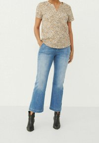 Blusa de manga corta con estampado floral en beige y blanco, combinada con unos vaqueros acampanados de color azul claro y botas negras de tobillo.