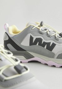 Baskets de sport gris clair avec des accents jaunes, en maille texturée et semelle en caoutchouc. Dotées de lacets ajustables et d'un logo noir bien visible sur le côté.