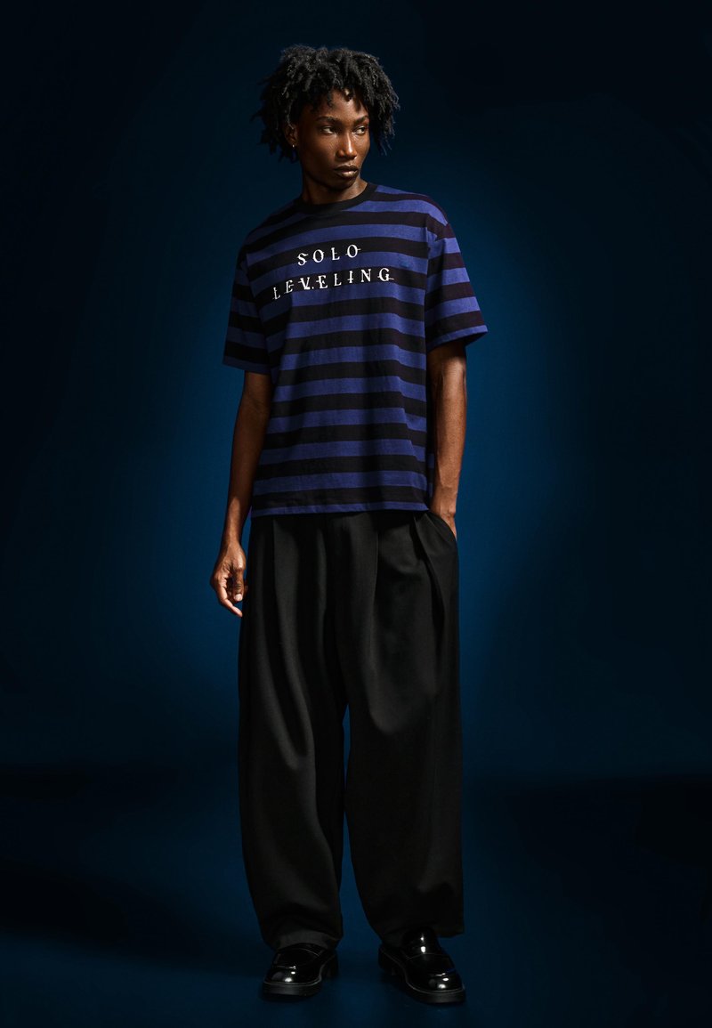 Modrý a černý pruhovaný tričko s bílým nápisem "SOLO LEVELING", doplněné volnými černými kalhotami a lesklými černými botami.