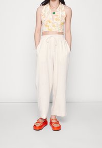 Crop top med blommönster i gult och orange, ihop med löst sittande krämfärgade byxor; klara röda platåsandaler med remmar.