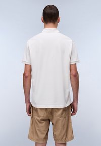 Kermakuvio polo paita lyhyillä hihoilla ja kauluksella, yhdistettynä khaki-shortsien kanssa. Kangas näyttää sileältä, ja saumat ovat näkyvissä, design-tiedot ovat minimaaliset.