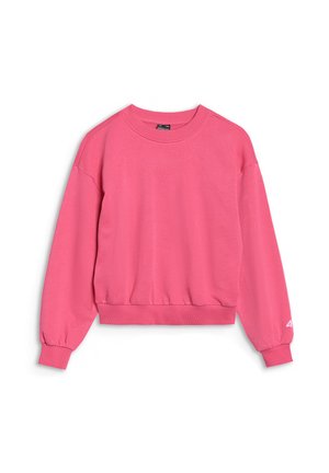 Jeune fille portant un sweat-shirt rose vif et un pantalon, les mains dans les poches, regardant légèrement à droite, portant une casquette sombre à l'envers.