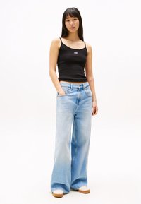 Light blue wide-leg jeans with a faded wash, paired with a fitted black tank top. Model stands in a neutral background.