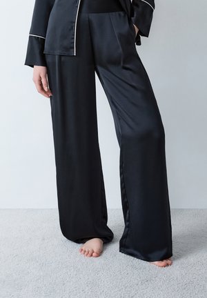 Pantalon de pyjama en satin noir avec une coupe large, présentant une texture lisse et une coupe décontractée, agrémenté de poches latérales.