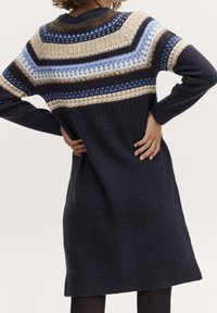 Stickad klänning i marinblått med flerfärgad geometrisk Fair Isle-mönster över axlarna. Långa ärmar, ribbade muddar och fåll.