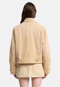 Beżowa kurtka jeansowa o luźnym kroju, z dużymi tylnymi kieszeniami, guzikami oraz wyraźnymi szwami. Tkanina o fakturze z jasnym wybarwieniem.