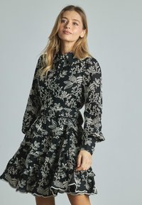Czarna sukienka z białym haftem kwiatowym, długie rękawy, guziki z przodu, falbaniasty dół oraz dopasowana talia. Lekki materiał, szczegółowy wzór.