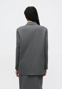Γκρι σακάκι με ραφή, με δομημένη σιλουέτα, μονή σχισμή και μανσέτες με κουμπιά. Λείο ύφασμα με διακριτική λάμψη και μινιμαλιστικό σχέδιο.