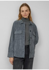 Gray corduroy jacket with a collared neckline, front button closure, and two patch pockets, worn over a fitted gray turtleneck.