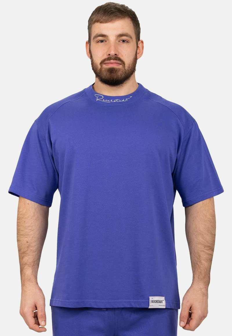 T-shirt court violet en coton léger, avec un col rond et un logo brodé en haut. Ourlet droit en bas.