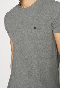 Grå kortærmet T-shirt lavet af blødt bomuld, med et lille rødt, hvidt og blåt emblem på brystet, rund halsudskæring og slim fit.