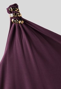 Tissu violet foncé rassemblé à un coin avec trois anneaux dorés brillants tenant les plis ensemble sur un fond neutre.