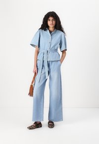 Light blue denim outfit with a short-sleeve button-up top and wide-leg pants, featuring a tie belt, paired with leopard-print shoes and a brown bag.