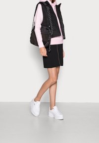 Gilet imbottito nero sopra un hoodie rosa, abbinato a una gonna nera. Sneakers bianche con plateau, maniche corte e dettagli con coulisse sul gilet.