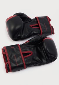 Μαύρα γάντια πυγμαχίας με κόκκινες λεπτομέρειες, κατασκευασμένα από συνθετικό δέρμα. Διαθέτουν ενισχυμένη ραφή και σταθερό ιμάντα στον καρπό για υποστήριξη. Μέγεθος 10 ουγγιές.