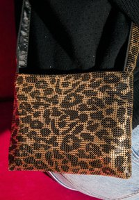 Auksinė ir juoda leopardų rašto rankinė su tekstūruotu paviršiumi, turinti ploną dirželį ir stačiakampį formą, atspariai prieš tamsų foną.