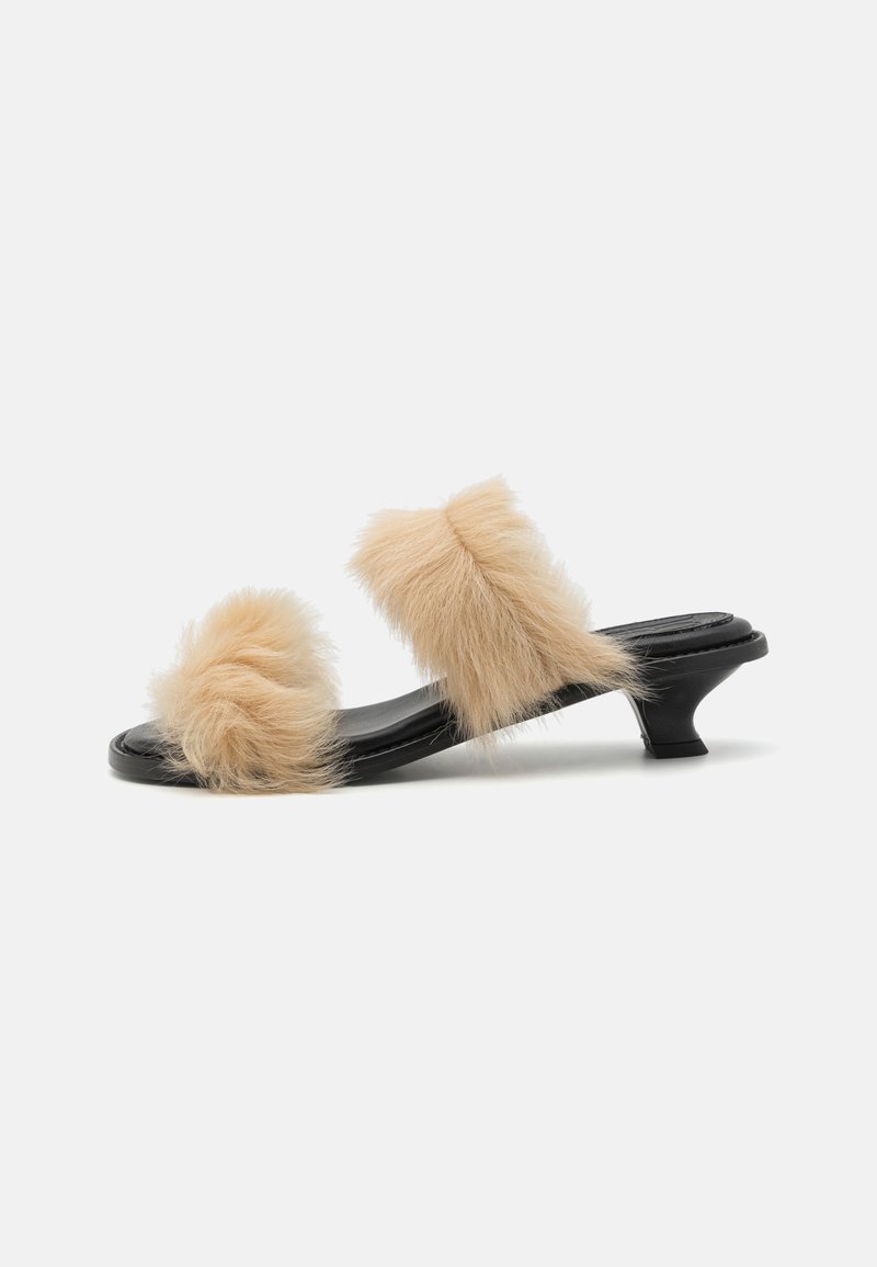 Black slide sandal with two beige faux fur pom-poms, low kitten heel, smooth surface, and open-toe design.