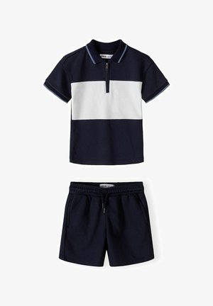 Marineblå og hvid kortærmet polo med lynlås, kombineret med marineblå elastiske shorts med snøre i taljen og lommer.
