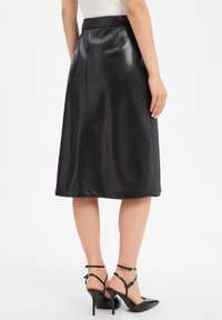 Jupe midi en cuir noir avec une texture lisse, dotée d'une taille simple et de coutures au dos, associée à des talons noirs à lanières.