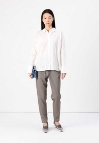 Vit, broderad skjorta med knappar och blommönster, kombinerad med grå byxor och metalliska loafers, hållande en blå clutch.