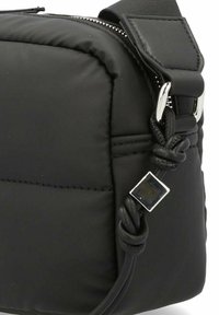 Borsa a spalla nera trapuntata con una texture liscia, chiusura con zip, dettaglio della tracolla intrecciata e un accento quadrato argentato sul lato.