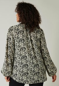 Sort blomster bluse med lange pufærmer, prydet med et cremefarvet blomstermønster og en rund kant. Stoffet virker let og struktureret.