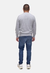 Maglione grigio chiaro con collo rotondo, abbinato a jeans blu. I jeans hanno due tasche posteriori con cuciture arancioni, indossati con sneaker bianche.