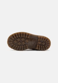 Suela de zapato de goma marrón con patrones de profunda tracción, diseños hexagonales y en cruz, y una superficie texturizada para mayor agarre.