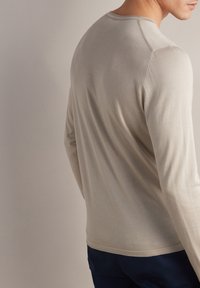 Beżowy sweter z długim rękawem i okrągłym dekoltem, wykonany z miękkiego materiału. Posiada dyskretne żebrowanie przy dekolcie oraz dopasowany krój.