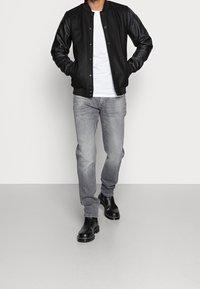 Chaqueta bomber negra con mangas de cuero, camiseta blanca debajo, jeans gris claro y botas de tobillo negras. Textura suave, cierre de botón.