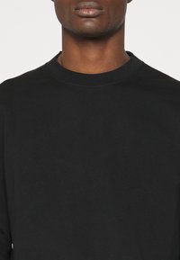 T-shirt nero a maniche lunghe realizzato in morbido cotone, caratterizzato da un colletto a girocollo e una superficie liscia, con dettagli di cucitura minimi.
