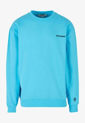 Sinine puuvillane dressipluus pikkade varrukatega, sooniku cuffid, ümar kaelus ja väike must logo rinnal. Sile tekstuur, mugav lõike.