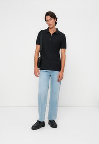 Melna zip-up polo krekls, gaiši zili taisni džinsi un melni sporta apavi. Vienkāršs dizains, brīva piegriezte un minimāls apdare.