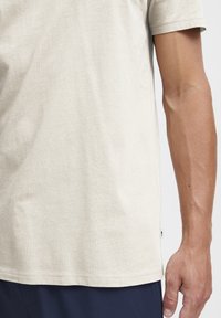 Beige kortærmet T-shirt lavet af blødt bomuld, med rund halsudskæring og diskrete syninger, samt et lille logomærke i siden.