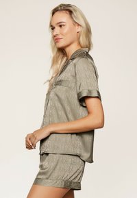 Svetlo maslinasto zeleni satenasti komplet pidžame s košuljom kratkih rukava s kragnom i džepom, te odgovarajućim šortsevima, oboje ukrašeno suptilnim uzorkom s logom.