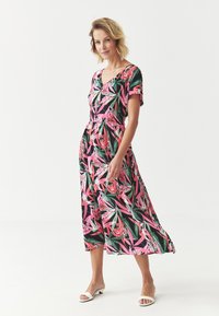 Robe midi florale en vert foncé, ornée de fleurs et feuilles roses. Manches courtes, décolleté en V, taille cintrée et jupe fluide.