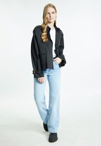 Zwarte cropped jack met zakken, gecombineerd met een witte T-shirt en lichtblauwe wijde jeans. Zwarte schoenen maken de outfit compleet.