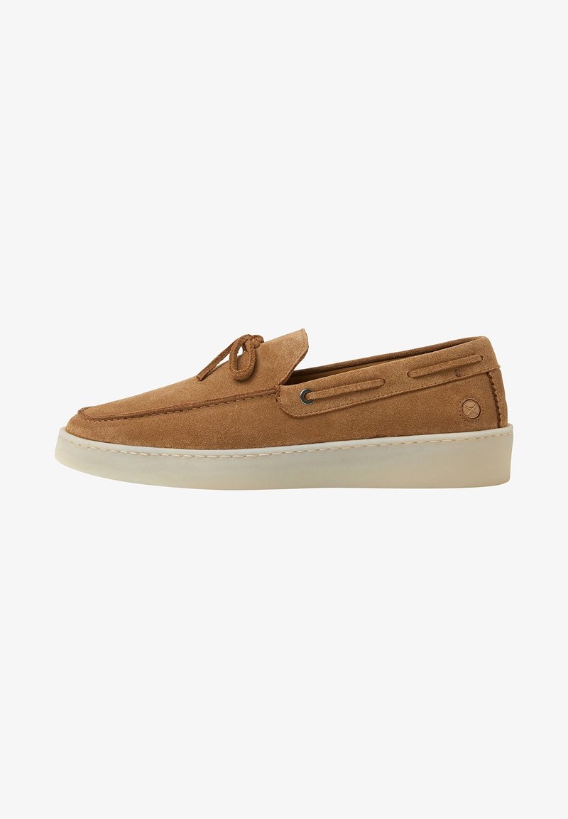 Chaussure à enfiler en daim marron avec une texture lisse, bout rond, et détail de lacet. Comprend une semelle en caoutchouc blanche et des accents de couture sur le côté.