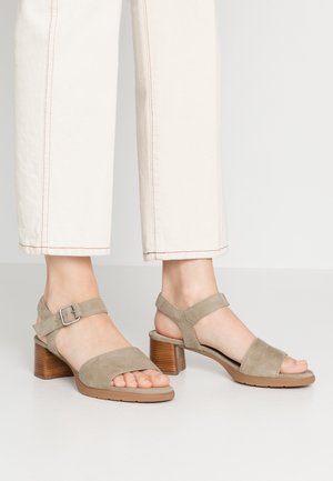 Beżowe zamszowe sandały na obcasie z paskiem wokół kostki, blokowym obcasem i otwartym noskiem, zestawione z kremowymi spodniami 3/4 z kontrastowym przeszyciem.