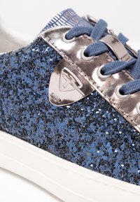 Baskets à paillettes bleues avec un accent métallique argenté sur la languette, des lacets en tissu, et une semelle en caoutchouc blanche. Tige texturée avec un effet scintillant.