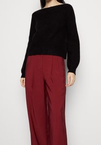 Svart ribbad stickad tröja med bred rundad halsringning, i kombination med löst sittande bordeauxfärgade byxor med framfållningar och en mjuk textur.