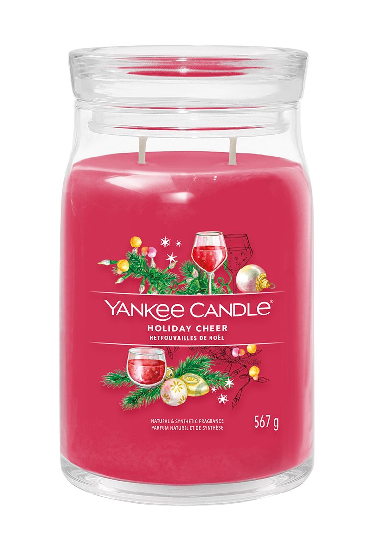 Giara rossa Yankee Candle etichettata "Festa Natalizia" con decorazioni festive tra cui rami di pino, ornamenti e bicchieri di vino rosso.