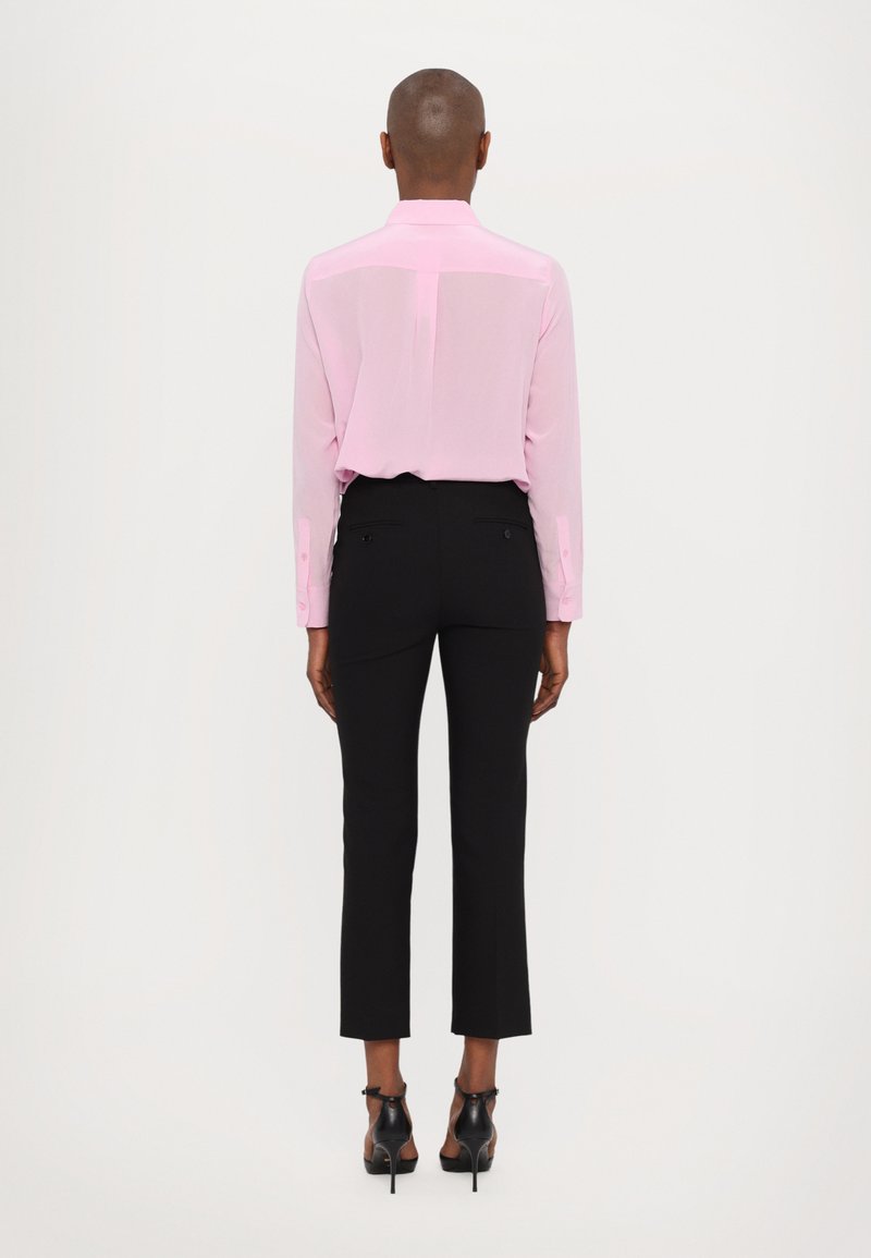 Jasnoróżowa, długorękawowa koszula z kołnierzykiem, zestawiona z czarnymi dopasowanymi spodniami i butami na obcasie. Gładki materiał i dopasowany krój.