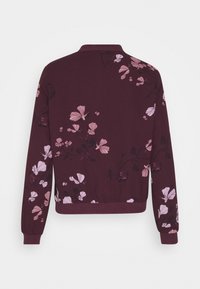 Bordeauxrode bomberjack met een bloemenprint in roze en wit, geribde kraag en manchetten, een aansluitende tailleband en een zachte stoftextuur.