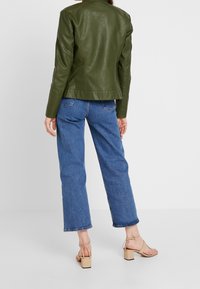 Giacca in pelle verde oliva con vestibilità su misura, abbinata a jeans a gamba dritta azzurri chiari e sandali beige con tacco a blocco.