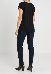 Top negro de manga corta con detalle de encaje, combinado con pantalones ajustados azul marino y botines marrones brillantes. Se aprecia la textura suave de la tela.