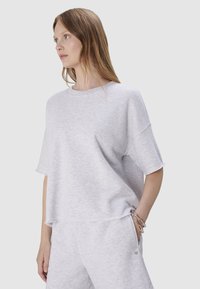 Jasnoszara, krótki rękaw, sweatshirt wykonany z miękkiego materiału, z luźnym krojem i prążkowanym dekoltem. Hem ma surowe krawędzie, co nadaje mu swobodny wygląd.